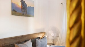 A hotel room with a bed, pillows, a nightstand, a fan, and a painting of a cow on a mountain. - Holiday Home 'Alpen Lodge' with Mountain View, Private Terrace and Wi-Fi (Garmisch-Partenkirchen)