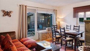 A living room with a sofa, a dining table with chairs, a fireplace, and a view through a sliding glass door. - Holiday Home 'Alpen Lodge' with Mountain View, Private Terrace and Wi-Fi (Garmisch-Partenkirchen)