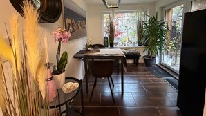 Un comedor con mesa, sillas, una araña y ventanas amplias con plantas.