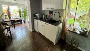 Cocina compacta con armarios blancos, encimera negra y ventana con vista a follaje.