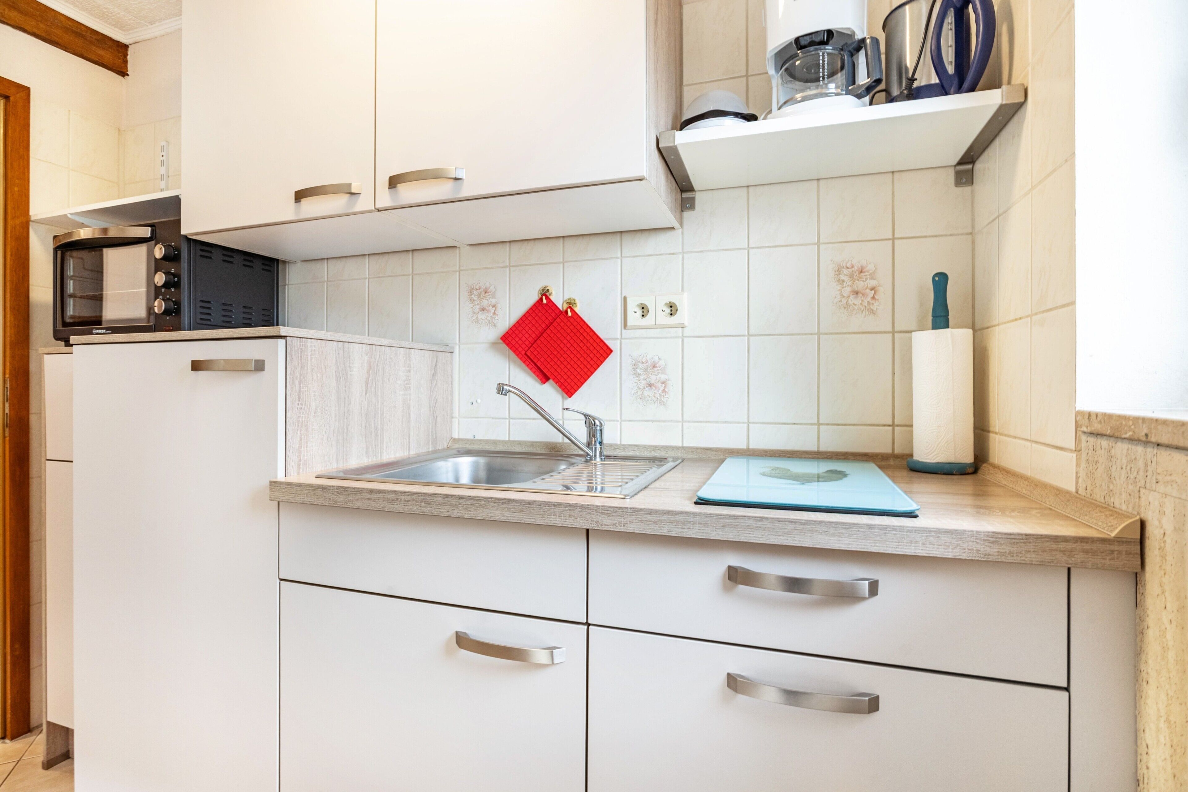 A modern kitchen with white cabinets, a stainless steel sink, a microwave, and a red kitchen towel.