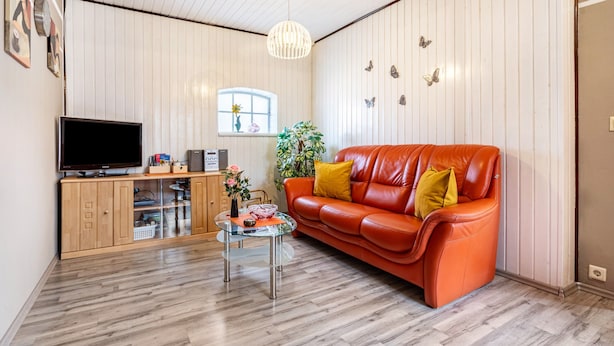 Una sala de estar con televisor, una mesa de centro de vidrio, un sofá de cuero rojo, armarios de madera y una ventana con planta.