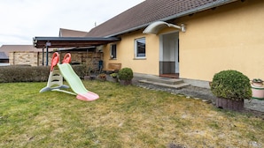 Un edificio residencial con un porche cubierto, un pequeño jardín y una zona de juegos con un tobogán.