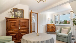 Una habitación con una mesa redonda, un armario de madera, un sillón verde y una ventana con vistas.