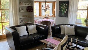 A living room with two black leather sofas, a white armchair, a wooden coffee table, and a chandelier.