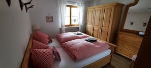 A bedroom with two beds, a wooden wardrobe, a window with curtains, and a wall-mounted picture.