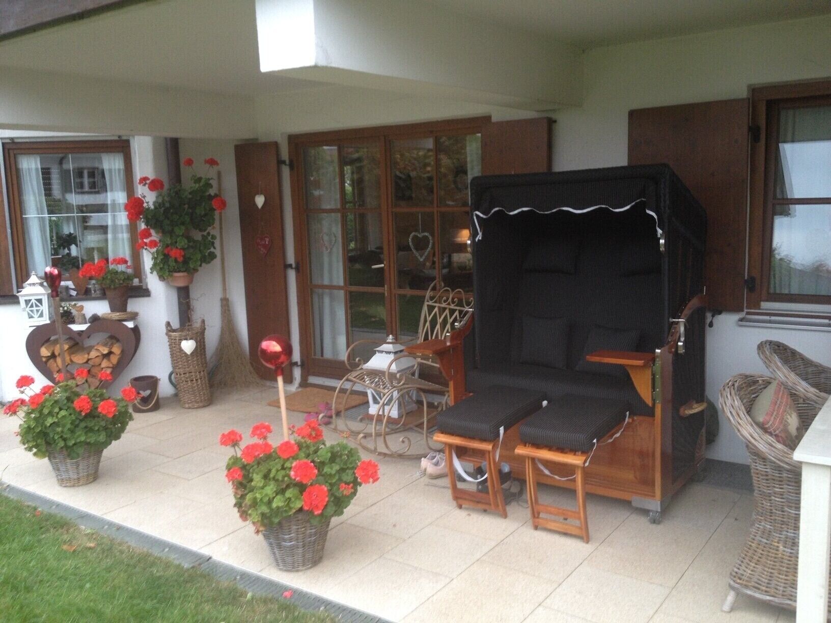 Een overdekt terras met buitenmeubilair, een barbecue en potplanten.