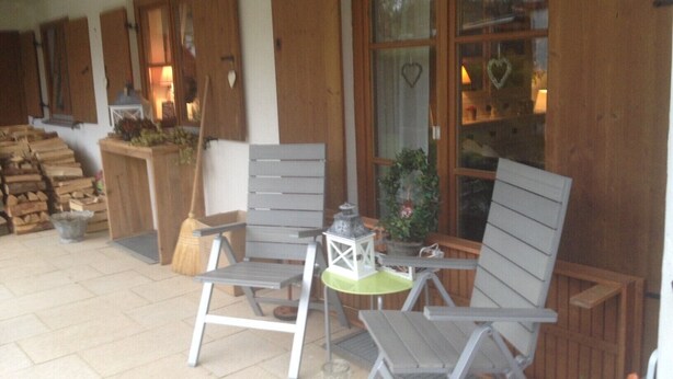 A covered outdoor seating area with wooden furniture, a lantern, and a potted plant.