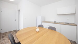 A modern, minimalistic room with a wooden dining table, two chairs, a white vase, a kitchen area with a sink and a refrigerator, and a white door. - Beautiful apartment in Vinjani Donji with WiFi (Vinjani Donji)