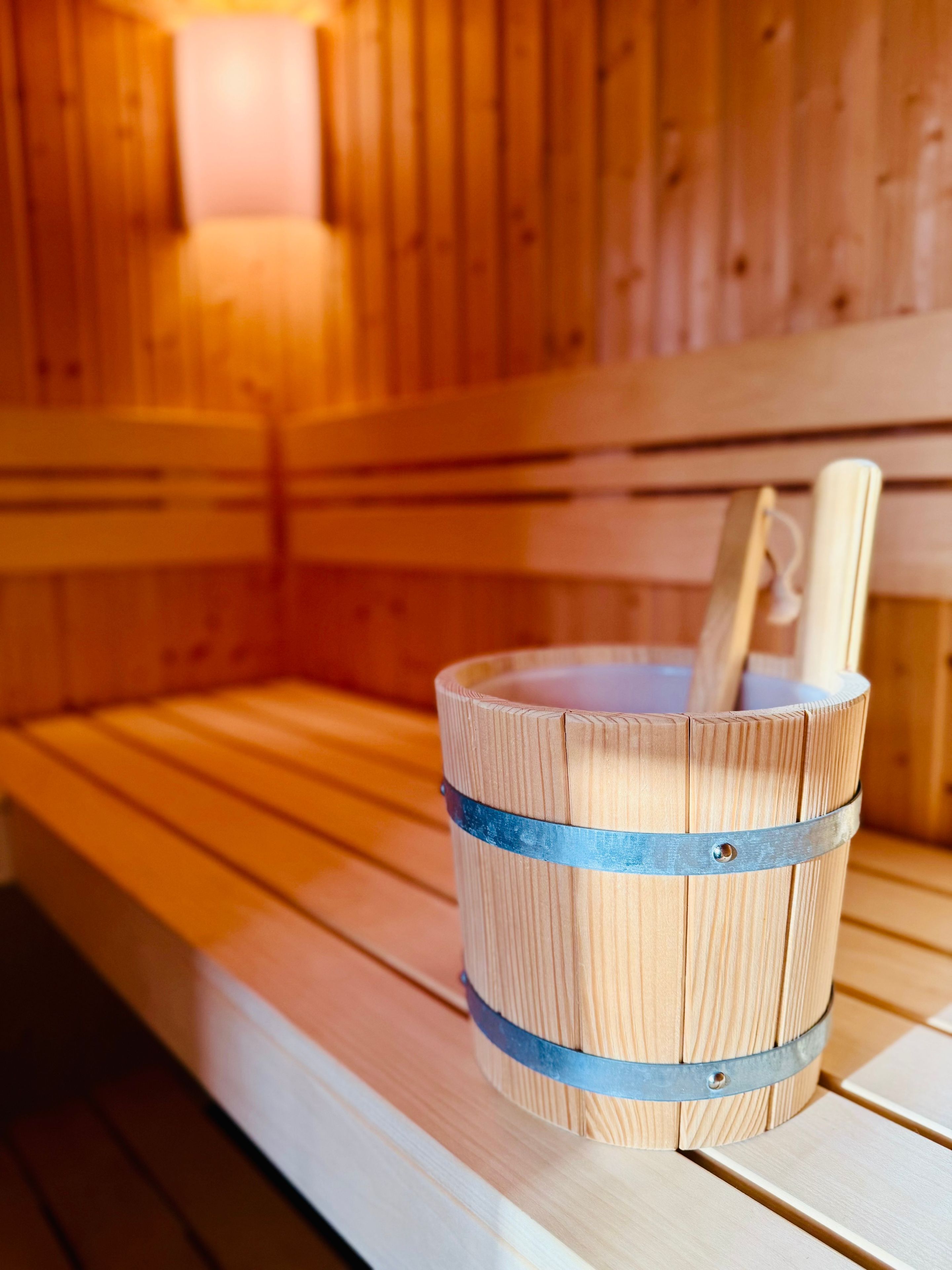 A wooden sauna bench with a metal bucket containing a wooden stick.