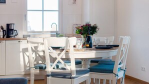 A dining area with white chairs, a round table, and a vase with flowers. - Holiday Home Mühlenperle with Private Terrace, Garden, Sauna & Parking, Baltic Sea, Stove (Boiensdorf OT Stove)