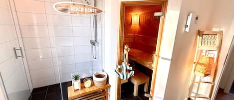 A bathroom with a shower, a wooden bench with a towel, and a small table with a plant and a basket.