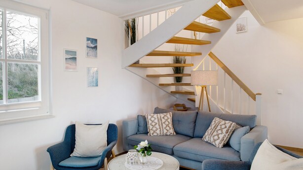 A modern living room with a blue sofa, a blue armchair, a round coffee table, and a wooden staircase. - Holiday Home Mühlenperle with Private Terrace, Garden, Sauna & Parking, Baltic Sea, Stove (Boiensdorf OT Stove)
