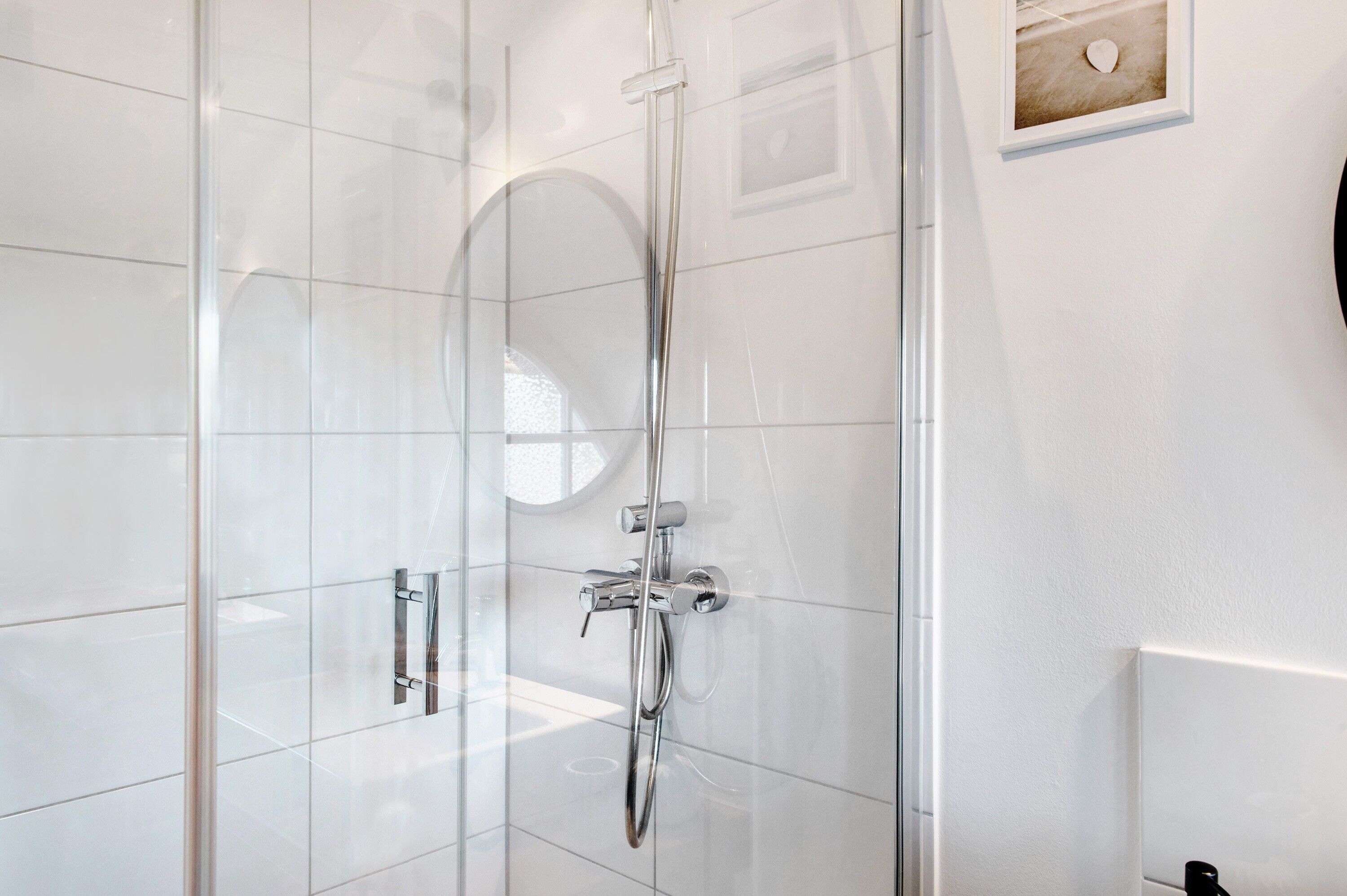 A modern shower with a glass enclosure, chrome fixtures, and a framed picture on the wall.