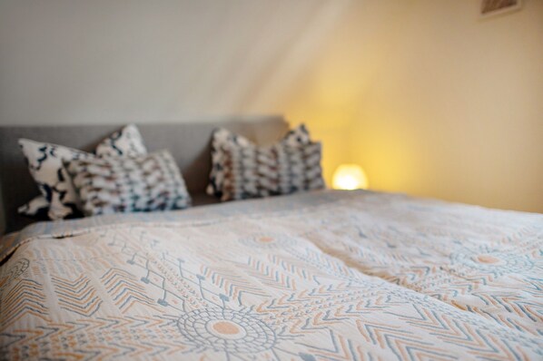 A neatly made bed with patterned bedding and pillows, a headboard, and a wall-mounted light fixture.