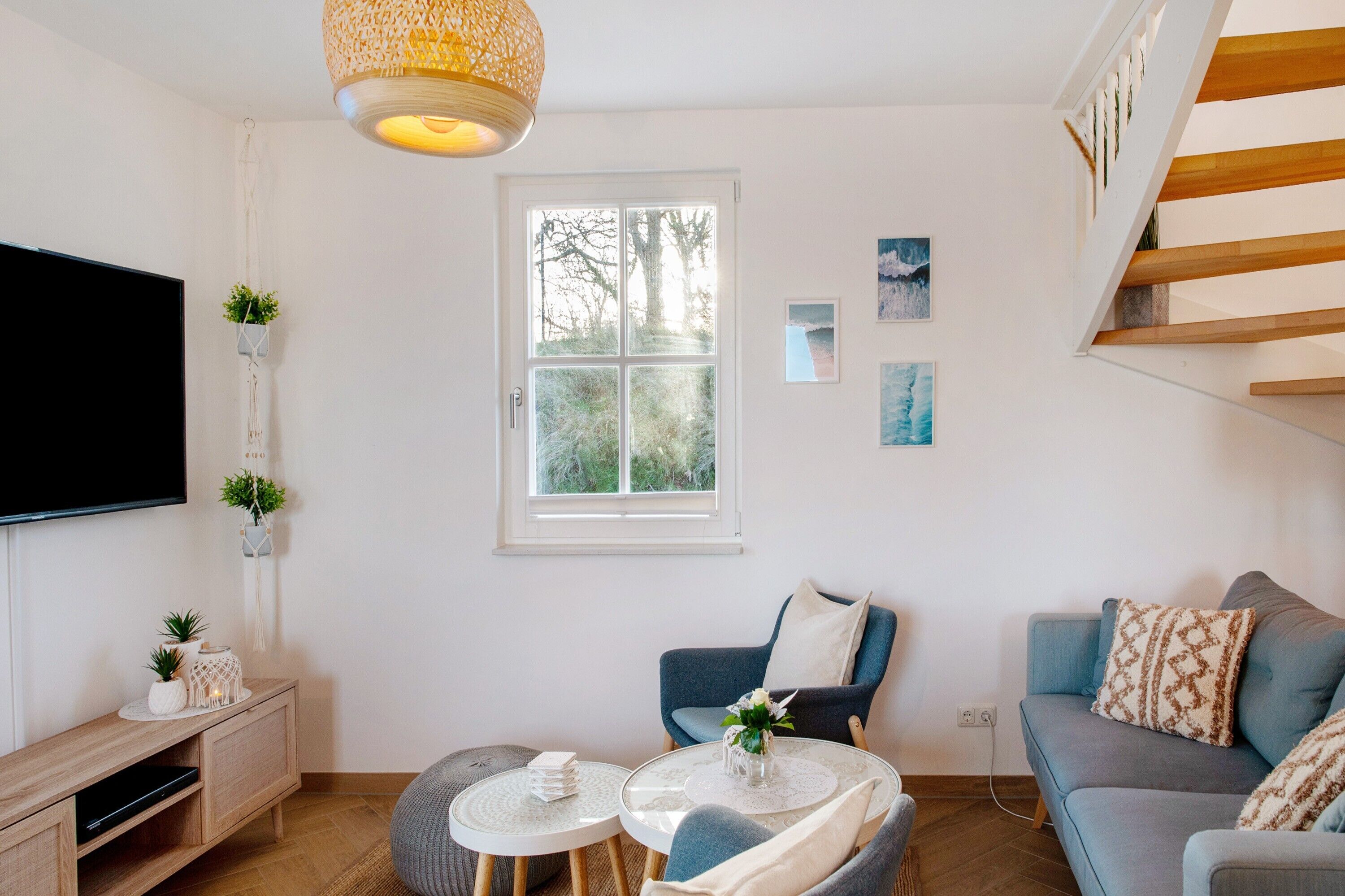 Een moderne woonkamer met een flatscreen televisie, een houten dressoir, een blauwe bank, een klein rond tafeltje en een raam met uitzicht op bomen.