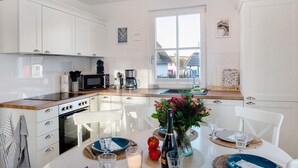 A modern kitchen with white cabinetry, a wooden countertop, and a dining area with a table set for two. - Holiday Home Mühlenperle with Private Terrace, Garden, Sauna & Parking, Baltic Sea, Stove (Boiensdorf OT Stove)