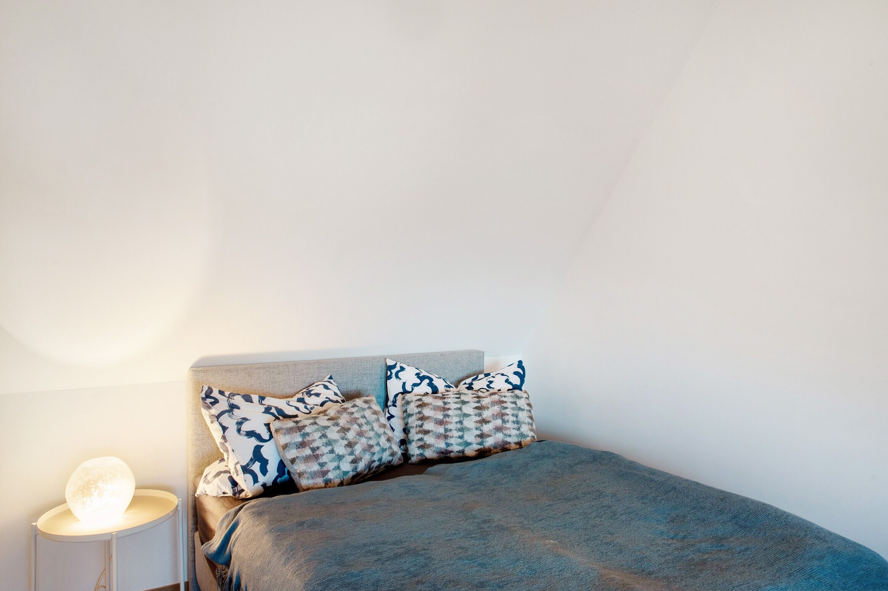 A bedroom with a bed, pillows, and a bedside lamp.