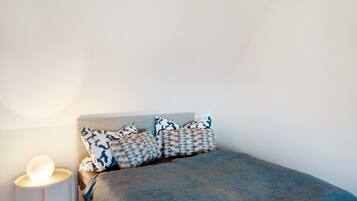 A bedroom with a bed, pillows, and a bedside lamp.
