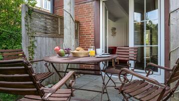 A patio with a table and chairs, a basket with fruits and a glass of juice, and a brick wall.