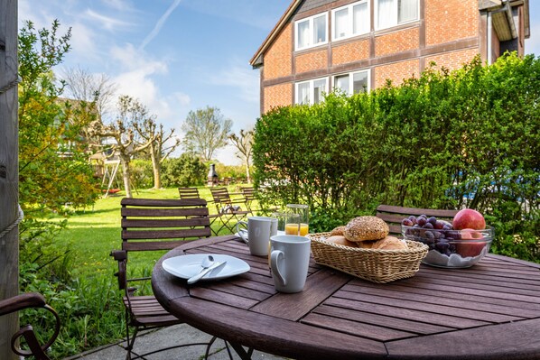 A round wooden table with breakfast items, a wicker basket, and a bowl of fruit.