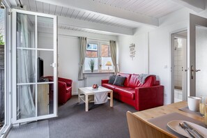Un salon avec un canapé rouge, une table basse en bois, une porte-fenêtre coulissante et une vue sur un immeuble en briques.