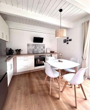 Une cuisine moderne avec des meubles blancs, un îlot central et un coin repas comprenant une table et des chaises blanches.