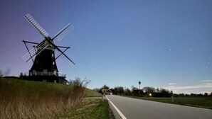 A windmill on a grassy hill beside a road.