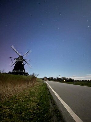 Un moulin à vent se dresse sur une colline herbeuse, au bord d’une route.