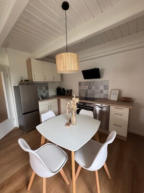 Une cuisine moderne avec des meubles blancs, une table à manger avec des chaises et un luminaire suspendu.