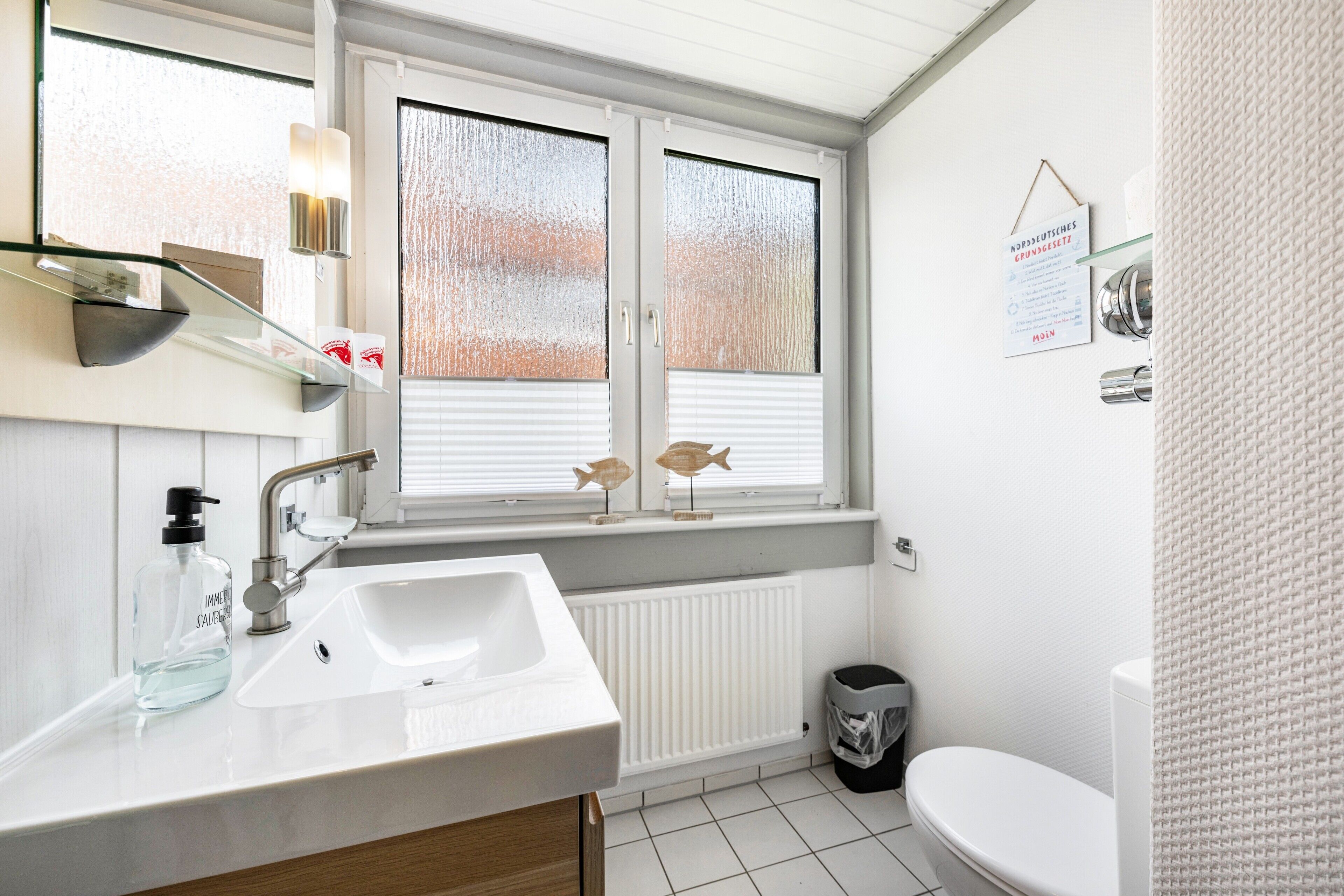 Ein Badezimmer mit einem weißen Waschbecken, einem Fenster mit Jalousien, einer Heizung und einer Toilette.