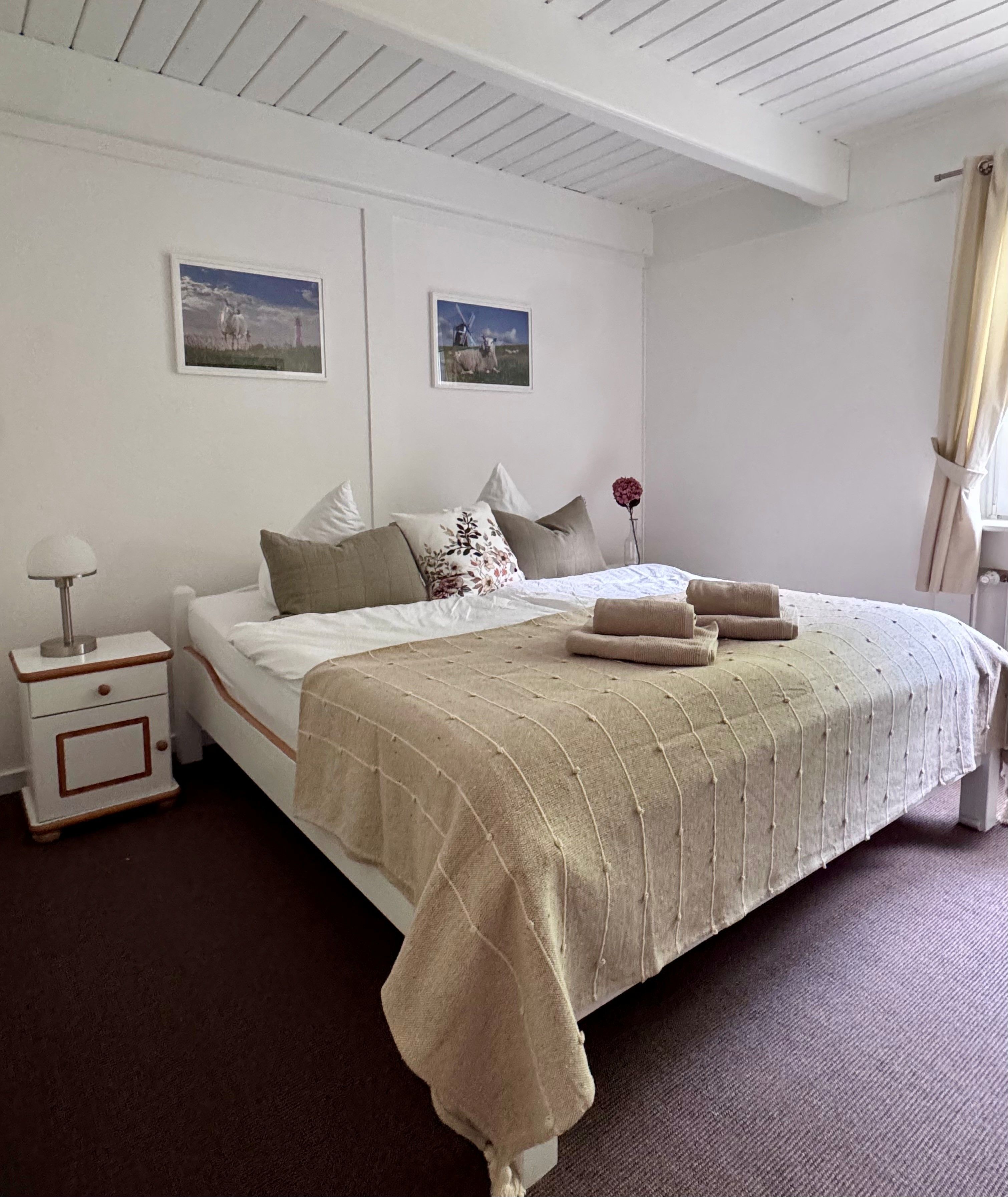 Una camera da letto ordinata con un letto, cuscini, un comodino e due quadri appesi al muro.
