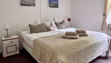 Una camera da letto ordinata con un letto, cuscini, un comodino e due quadri appesi al muro.