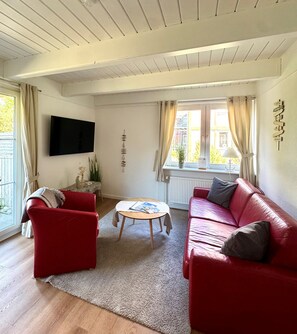 Un salon avec un canapé rouge, un fauteuil rouge, une table basse en bois et un téléviseur à écran plat fixé au mur.