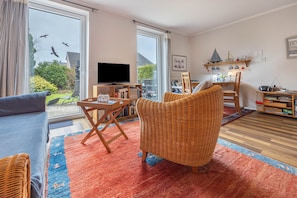 A living room with a television, wicker furniture, a bookshelf, and a view of the outdoors.