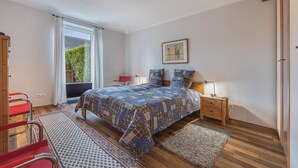 A bedroom with a bed, bedside tables, a window with curtains, a chair, and a small rug. - Apartment 'Haus Erika' with Shared Terrace, Shared Garden and Wi-Fi (Brunsbüttel)