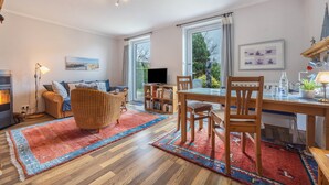 A modern living room with a fireplace, a dining area with wooden furniture, and large windows offering a view of the outdoors. - Apartment 'Haus Erika' with Shared Terrace, Shared Garden and Wi-Fi (Brunsbüttel)