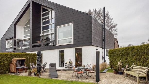 A modern house with a sloped roof, large windows, and a patio area with outdoor furniture. - Apartment 'Haus Erika' with Shared Terrace, Shared Garden and Wi-Fi (Brunsbüttel)