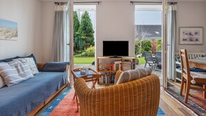 A living room with a sofa, a wicker chair, a TV, and a bookshelf. - Apartment 'Haus Erika' with Shared Terrace, Shared Garden and Wi-Fi (Brunsbüttel)