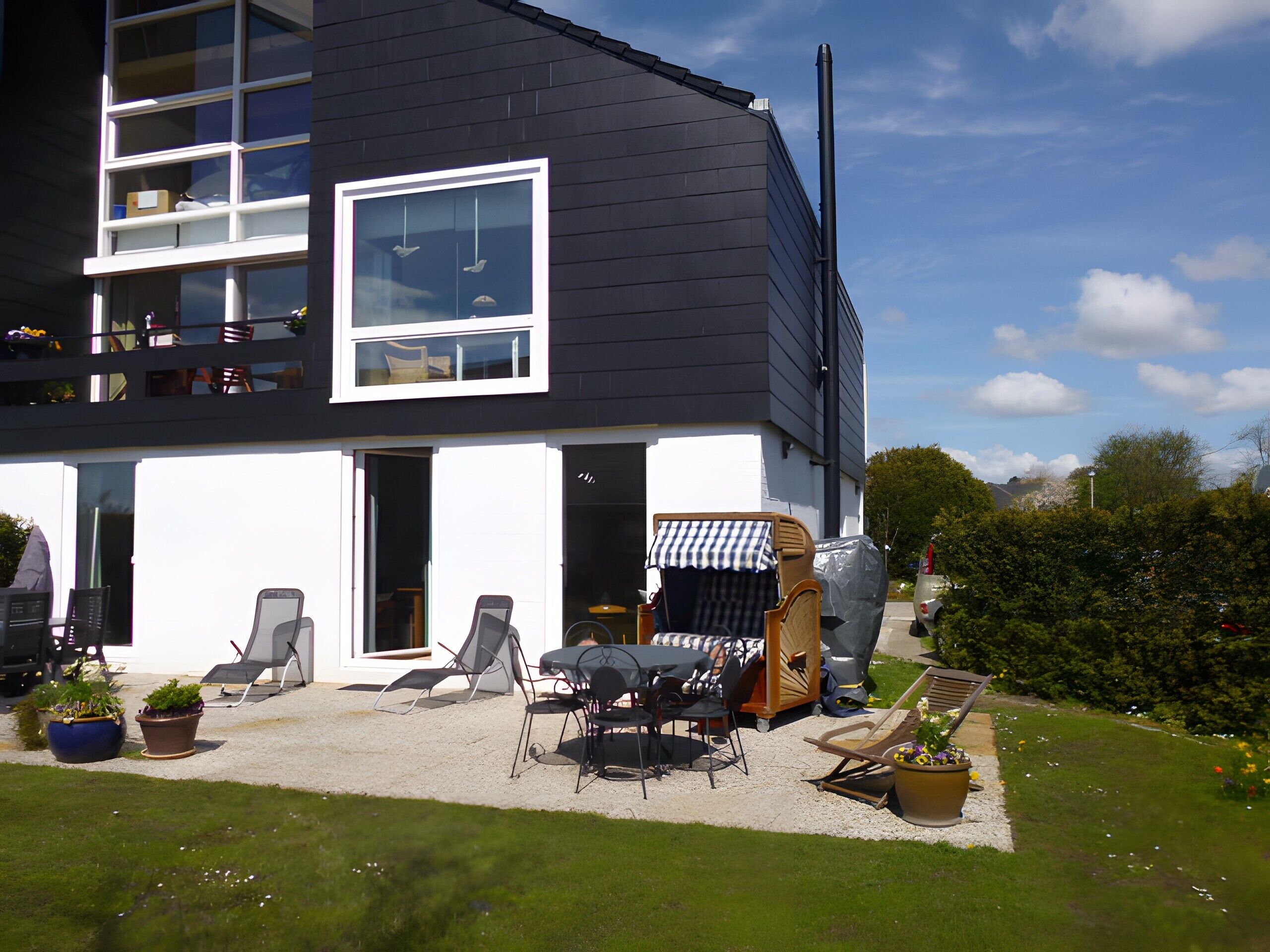 Een modern huis met twee verdiepingen, een balkon, buitenmeubilair en een overdekte patio.