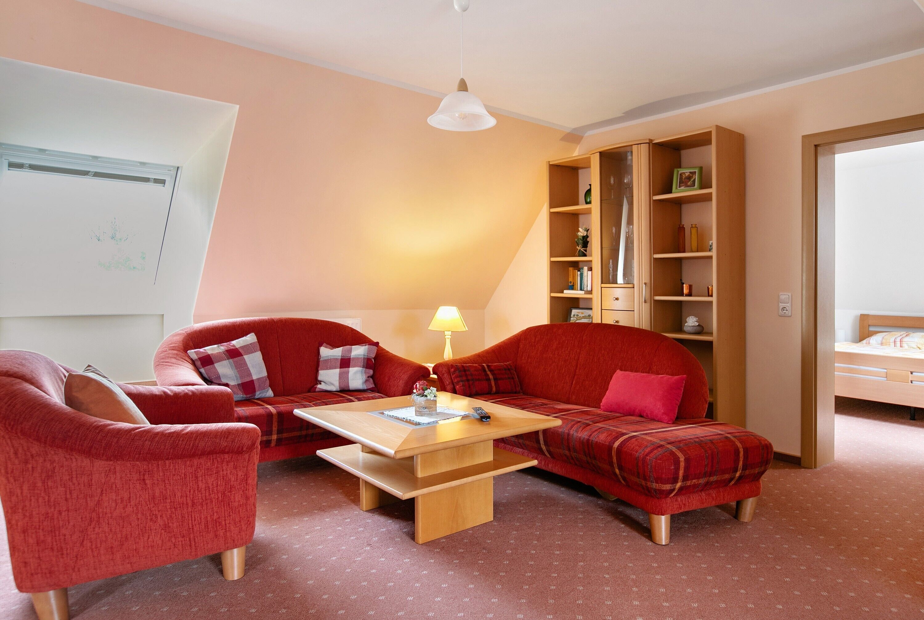 A room with a red sofa, a wooden coffee table, a bookshelf, and a bed.