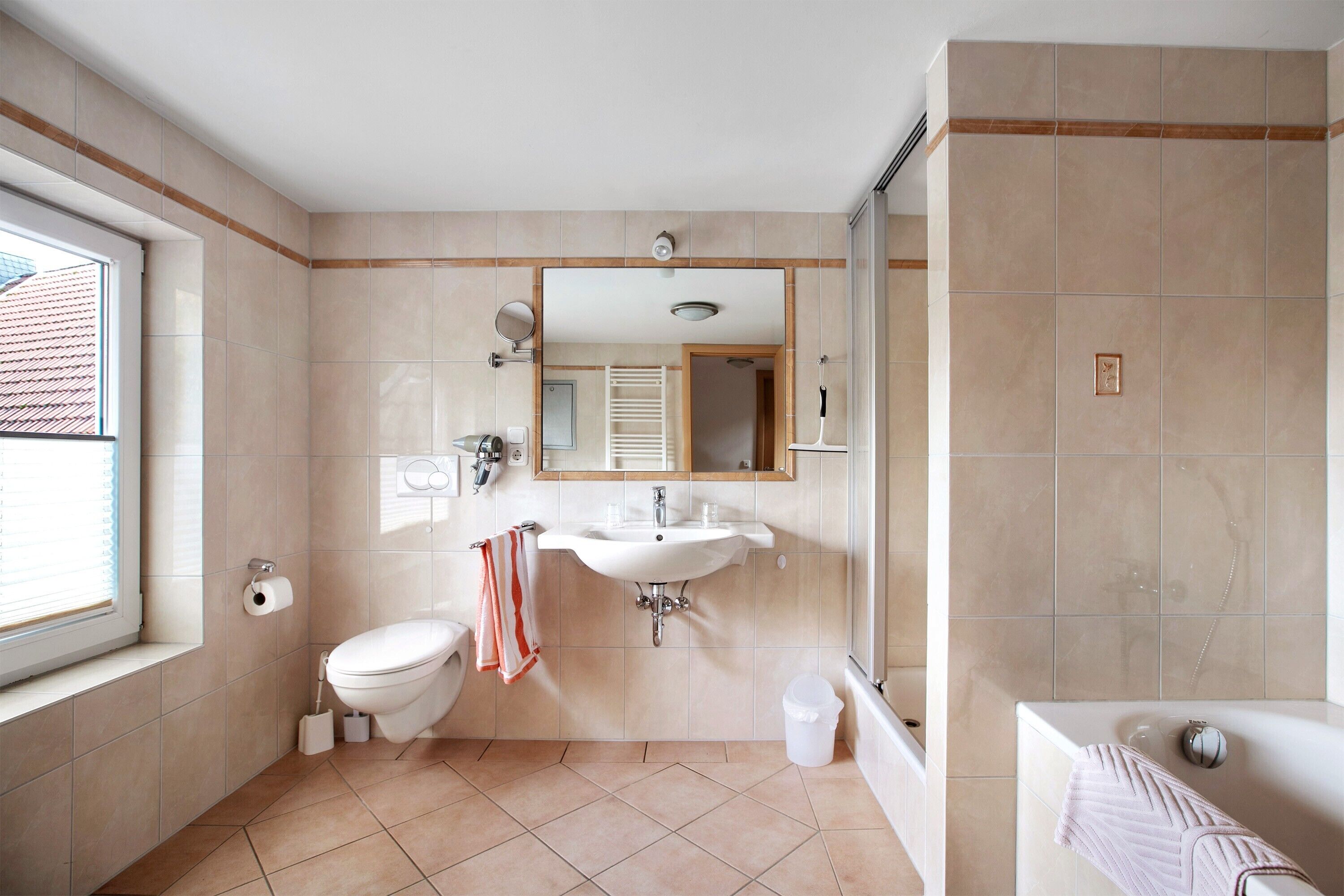 A bathroom with a toilet, sink, mirror, shower, and a window.