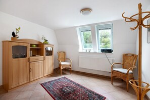 Una habitación con un armario de madera, dos sillas de mimbre, un tapete estampado y una ventana con vistas a zonas verdes.