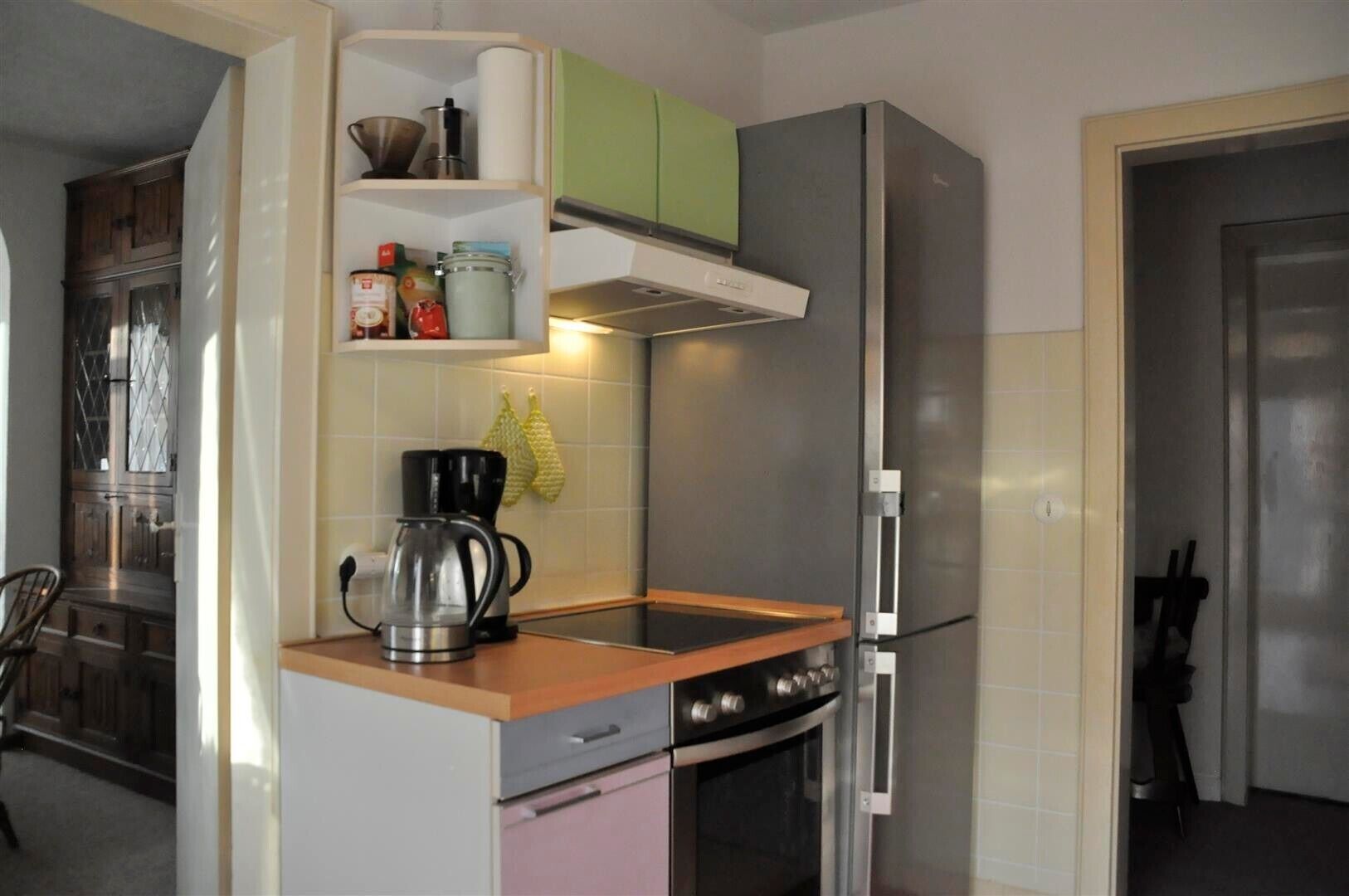A compact kitchen with a built-in oven, a coffee maker, and a shelf with kitchen items.
