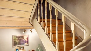 Una escalera de madera con balaustres blancos, un estante con adornos y un cuadro en la pared.