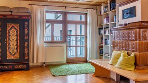 Una habitación con techo de madera, un ventanal con vistas, un radiador, una alfombra verde y una estantería.