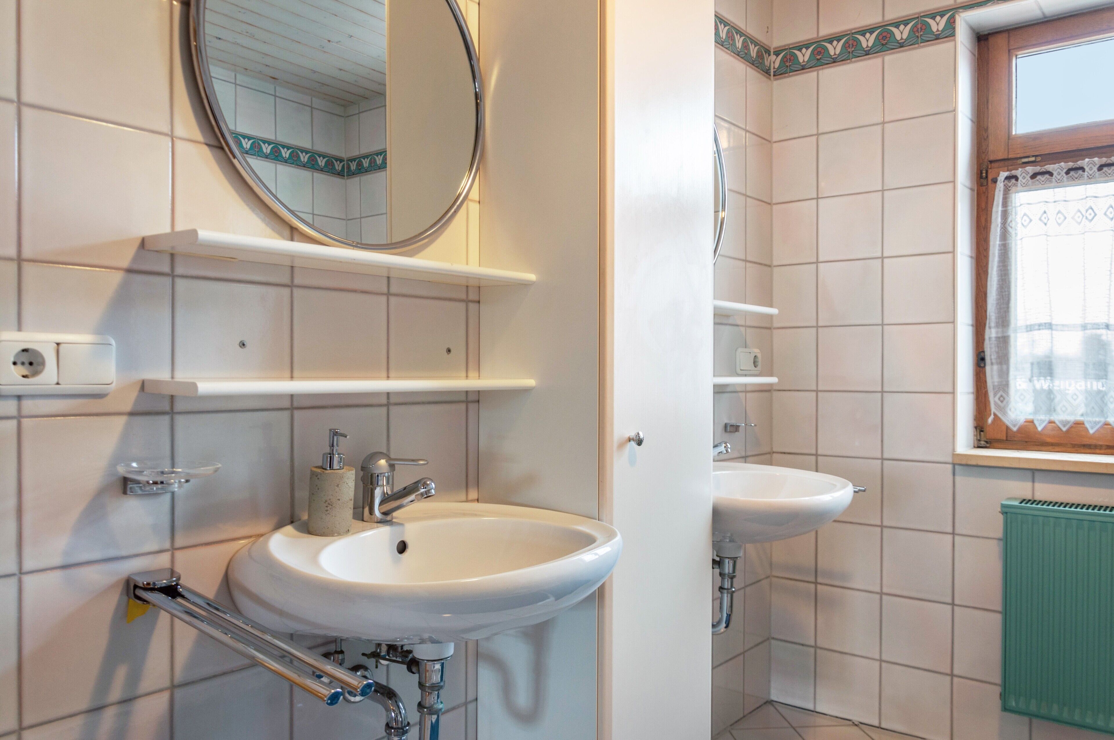 A bathroom with two sinks, a mirror, and a window with a curtain.