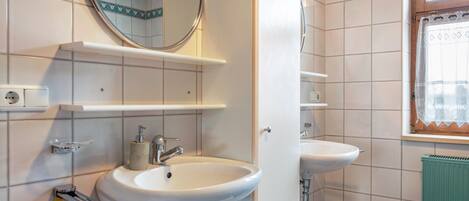 A bathroom with two sinks, a mirror, and a window with a curtain.