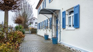 Un estrecho sendero pavimentado que conduce a un edificio con contraventanas azules y plantas en macetas.