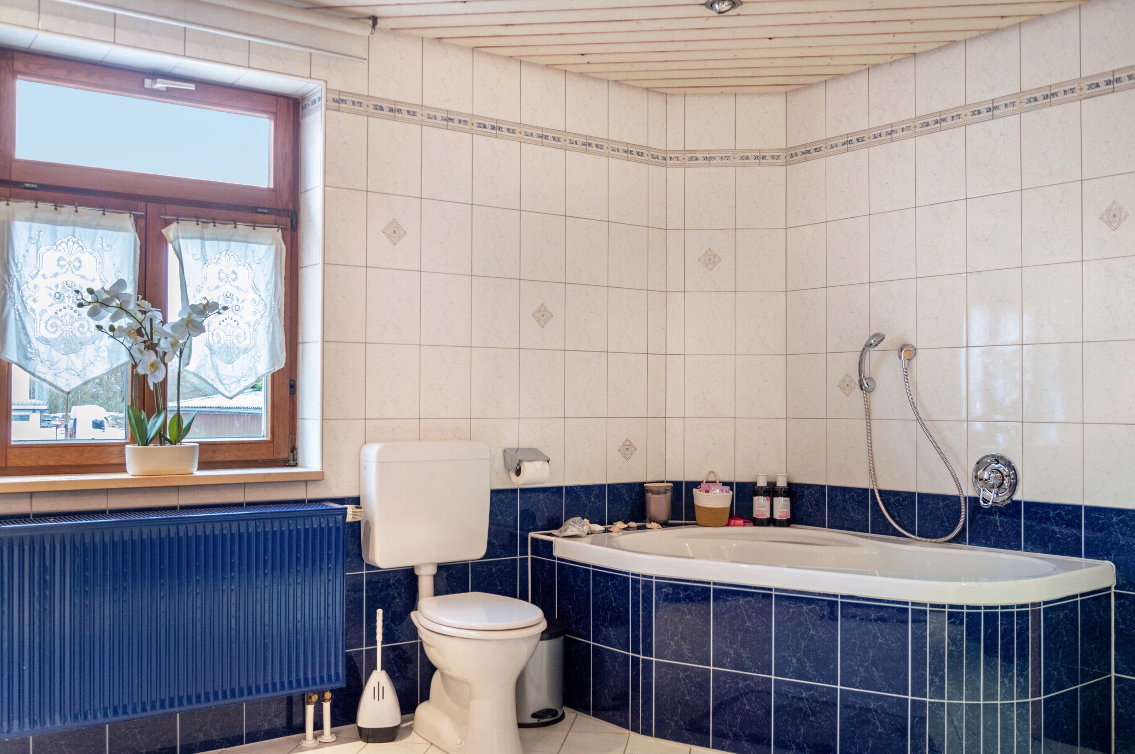 A bathroom with a toilet, a bathtub, a window with curtains, and a radiator.
